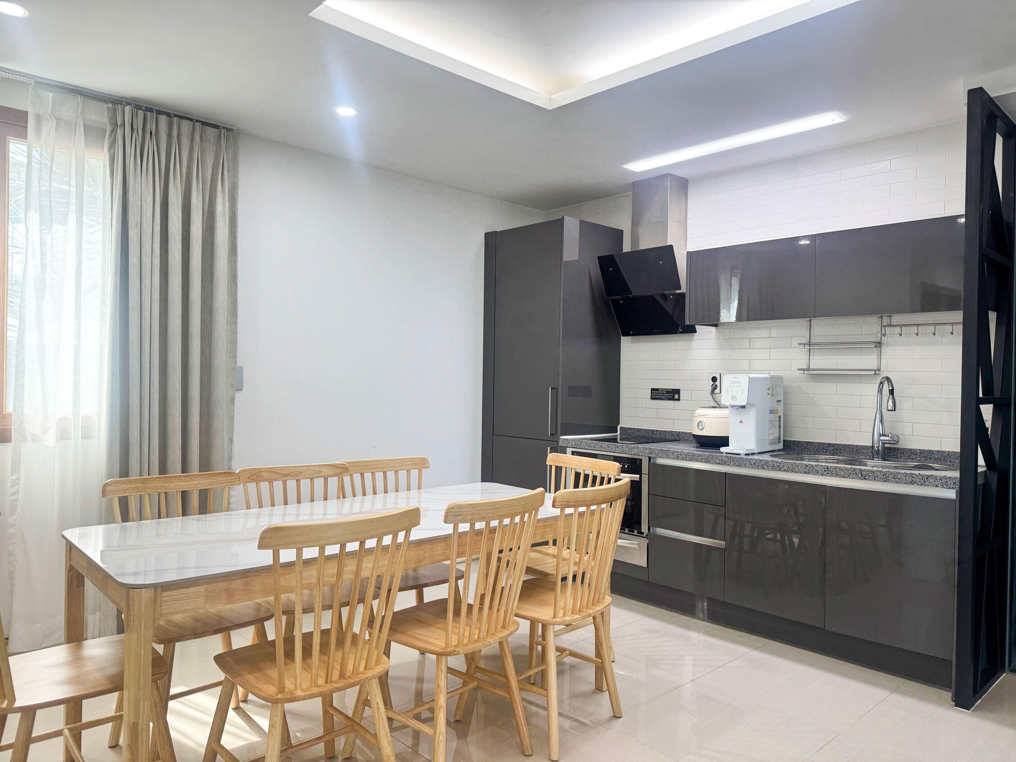 Una cocina moderna con una mesa de comedor y sillas, horno empotrado y un lavamanos de acero inoxidable.