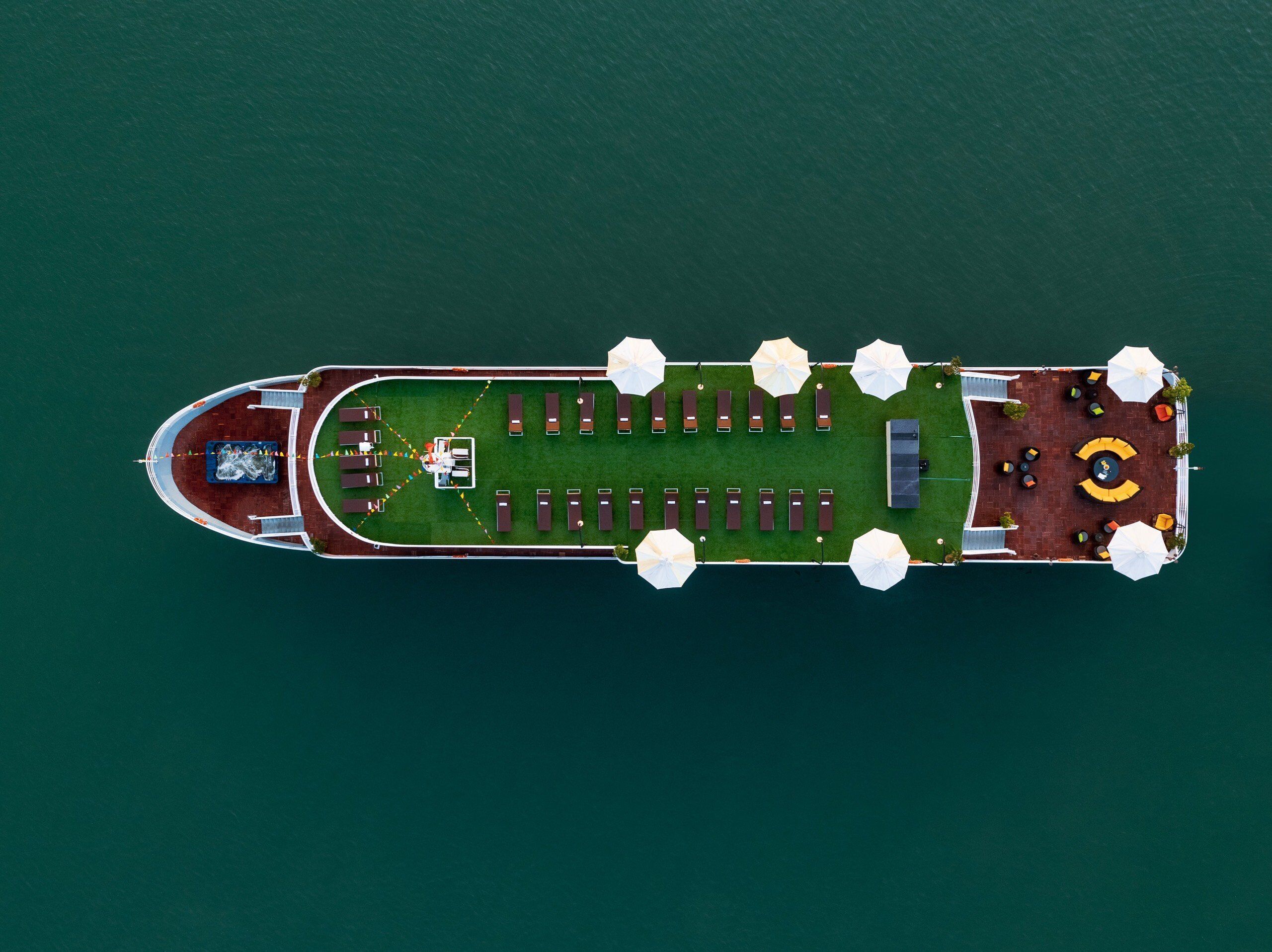An aerial view of a cruise ship with a deck area featuring rows of sun loungers, umbrellas, and a central seating area.