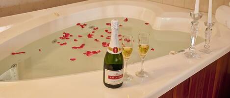 A bathtub with rose petals, champagne, and glasses, suggesting a romantic setting.