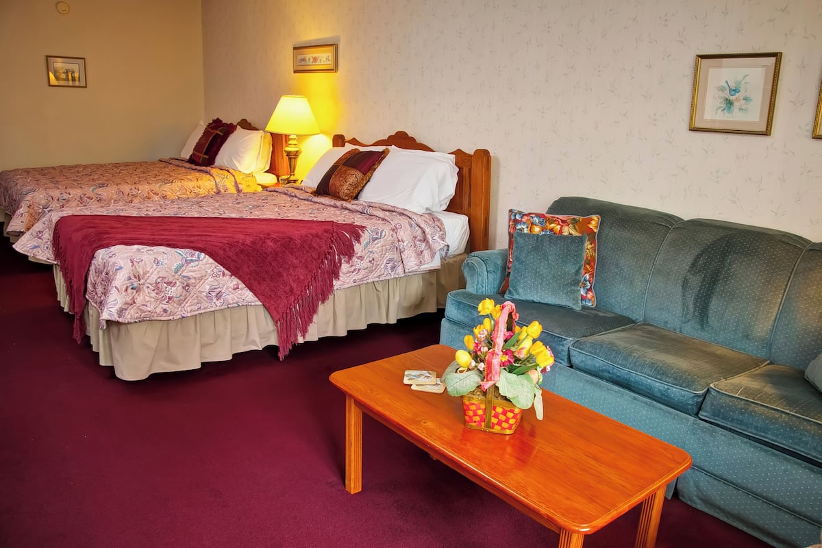 A hotel room with two beds, a blue sofa, a wooden coffee table, and a lamp.