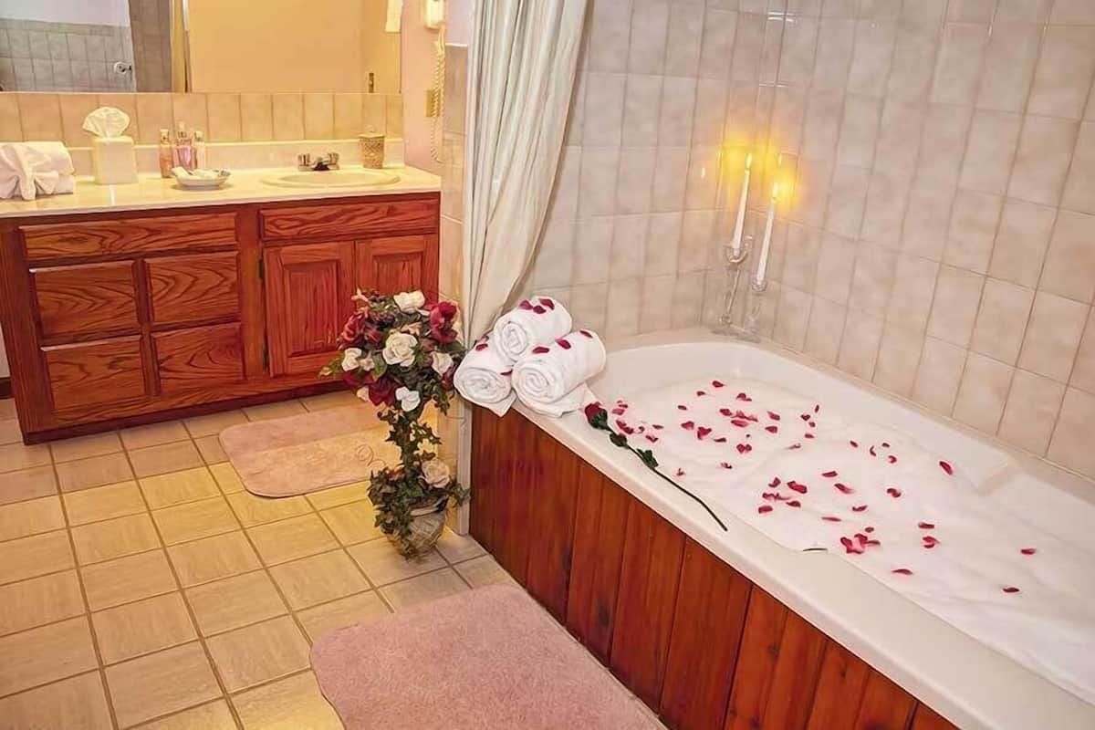 A bathroom with a wooden vanity, a bathtub with rose petals, and a potted plant.