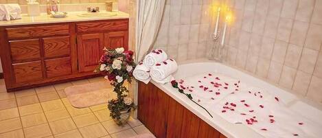 A bathroom with a wooden vanity, a bathtub with rose petals, and a potted plant.