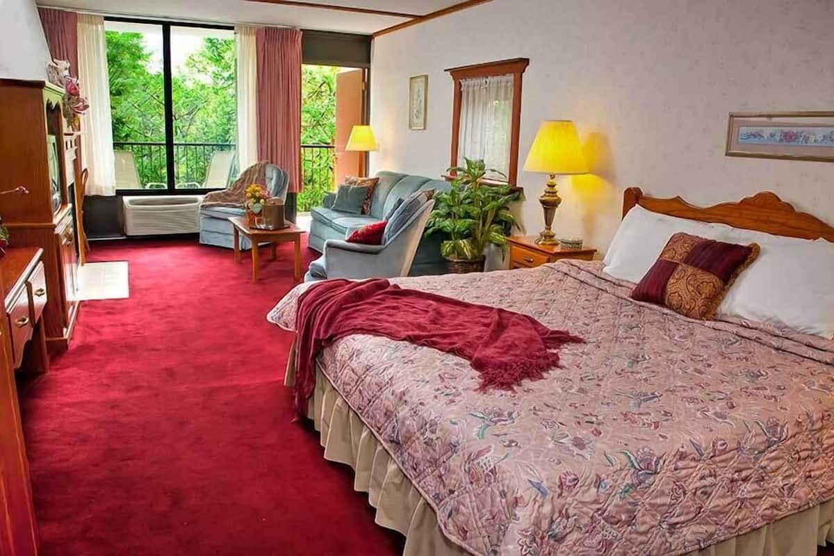 A bedroom with a large bed, a chair, a small table, a lamp, and a window with curtains.