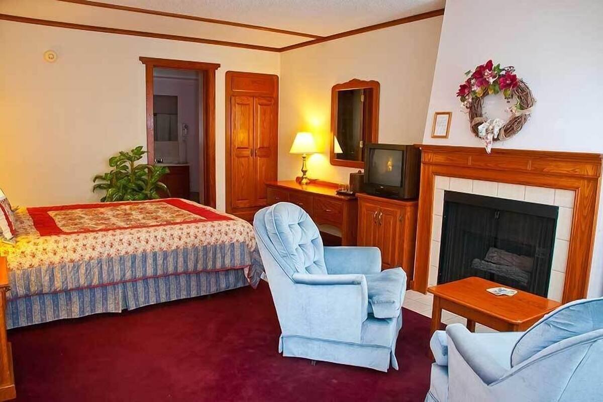 A room with a bed, two armchairs, a television, a fireplace, and a mirror.