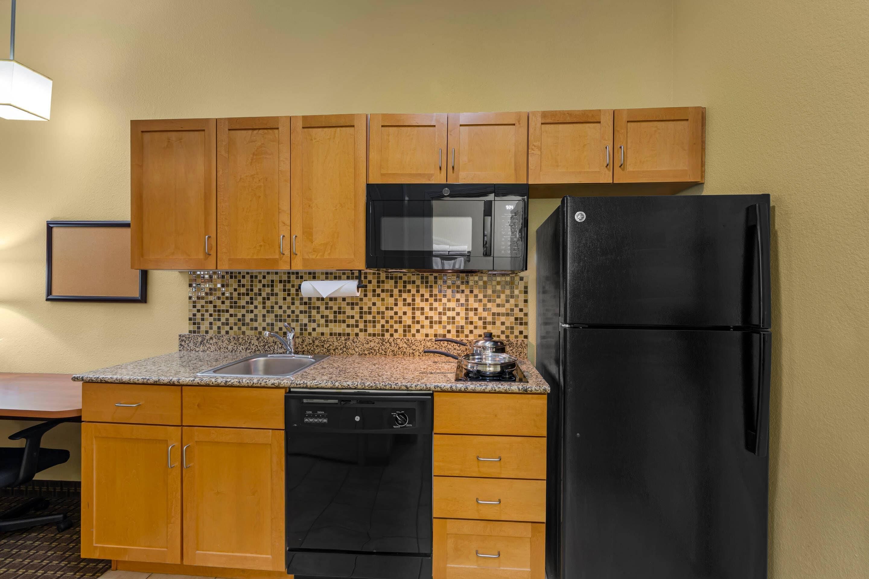 A compact kitchen with wooden cabinets, a black microwave, a black refrigerator, and a dishwasher.