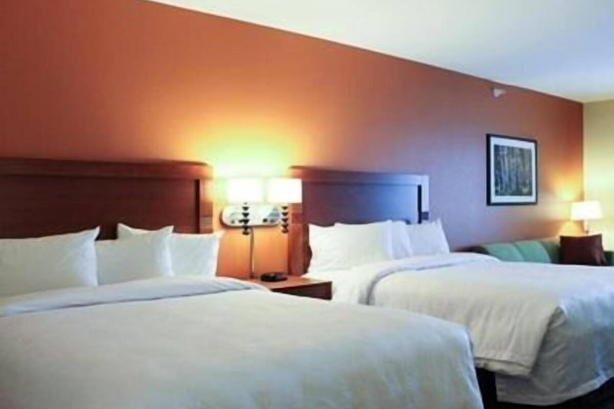 A hotel room with two beds, a nightstand, a lamp, and a framed picture on the wall.