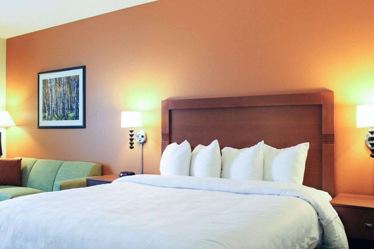 A hotel room with a large bed, two bedside lamps, a nightstand, a green armchair, and a framed picture on the wall.