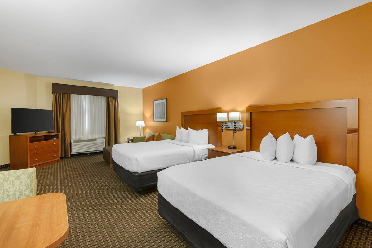 A hotel room with two beds, a TV, a desk, and a window with curtains.
