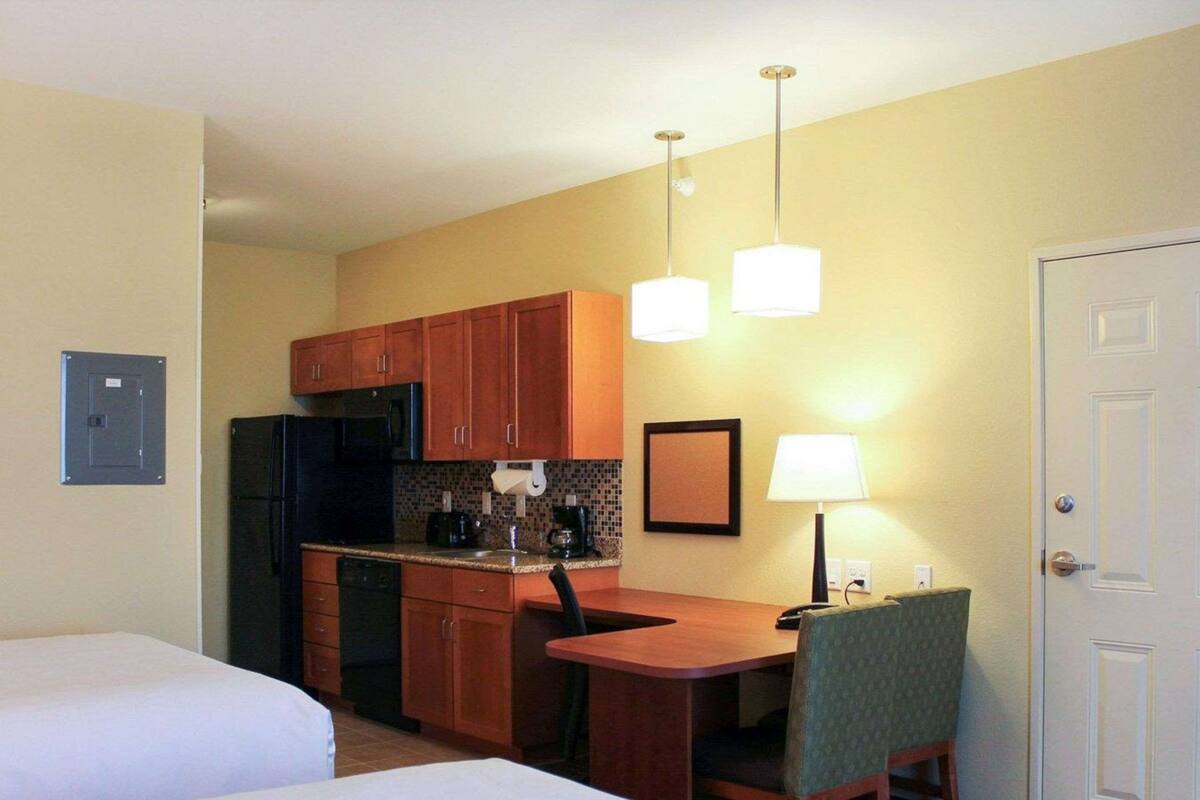 A hotel room with two beds, a kitchenette, a dining table with a chair, and a door.