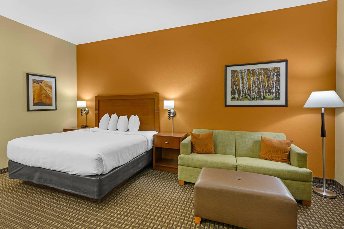 A hotel room with a large bed, a green sofa, a small table, and a floor lamp.