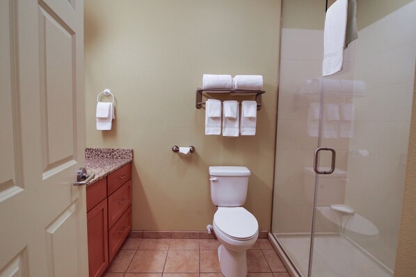 A bathroom with a toilet, a towel rack with multiple towels, a shower area, and a door with a handle.