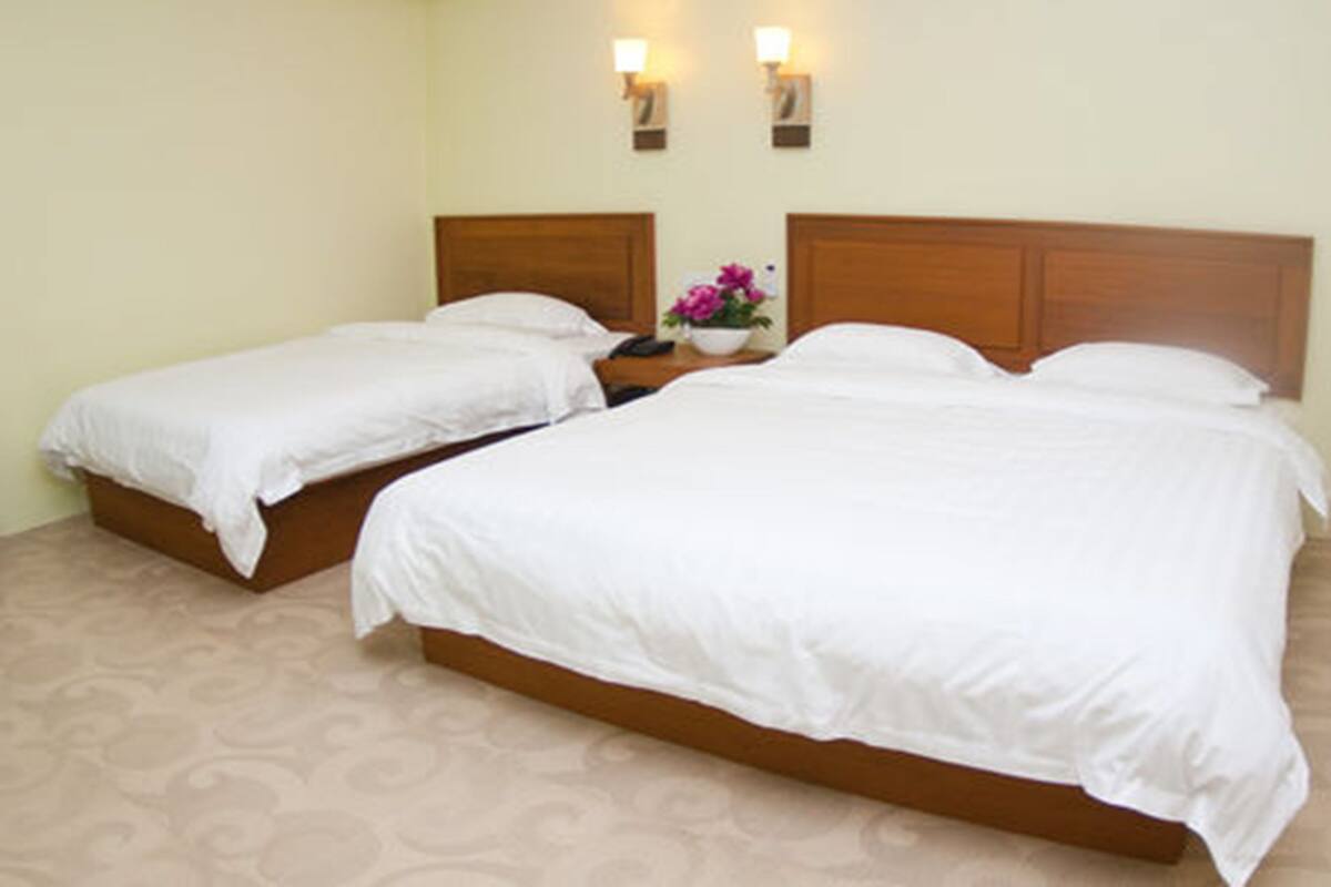 Habitación de hotel con dos camas individuales y una cama doble, una mesita de noche con un florero, y lámparas fijadas a la pared.