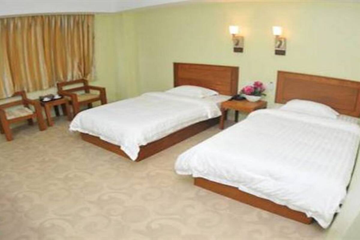 Habitación de hotel con dos camas individuales, una mesita con una lámpara, una silla y una ventana con cortinas.