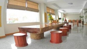 Un vestíbulo amplio con un largo mostrador de recepción de madera, varias sillas de madera y un gran ventanal con persianas.