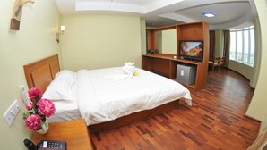 Una habitación de hotel con una cama, televisión, escritorio con teléfono y un florero.