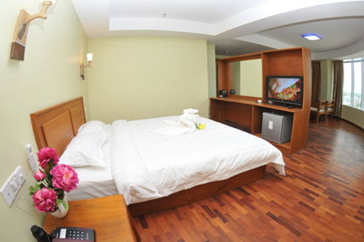 Una habitación de hotel con una cama, televisión, escritorio con teléfono y un florero.