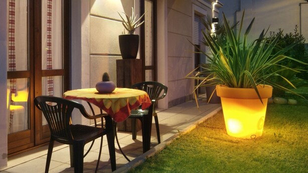 An outdoor dining area with a table and chairs, potted plants, and a well-lit balcony. - Residenza Il Fiore (Bergamo)
