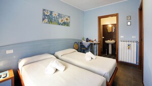 A hotel room with two beds, a small table with a mirror, a sink, and a painting of flowers on the wall. - Residenza Il Fiore (Bergamo)