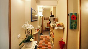 A narrow hallway with a patterned rug, a small table with a vase of flowers, and a painting on the wall. - Residenza Il Fiore (Bergamo)