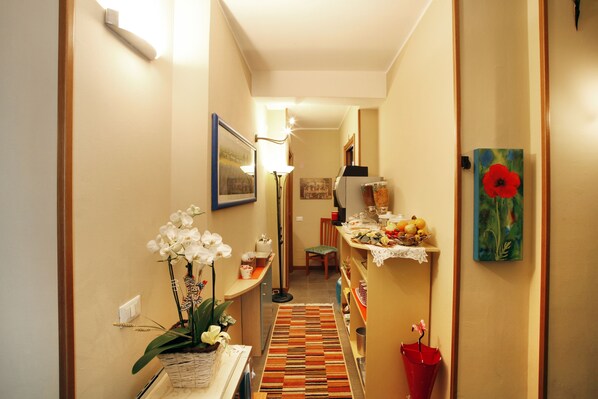 A narrow hallway with a patterned rug, a small table with a vase of flowers, and a painting on the wall. - Residenza Il Fiore (Bergamo)