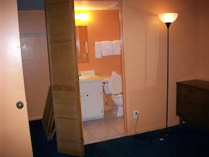 Un baño con inodoro, lavabo y una toalla colgada en la pared. Una puerta de madera da a otra habitación.