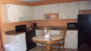 A compact kitchen with white cabinets, a microwave, a coffee maker, and a dining table with chairs. - All Suite Motel (Edgewater)