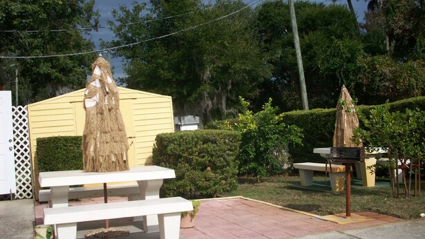 A patio area with a white bench, a small table, and a thatched umbrella. - All Suite Motel (Edgewater)