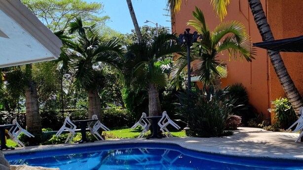 Piscina com água azul cristalina, cercada por palmeiras e um deck revestido com azulejos.