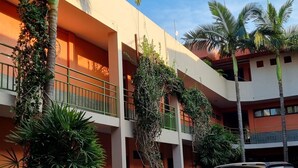 Um edifício de vários andares com varandas, rodeado por palmeiras e vegetação.