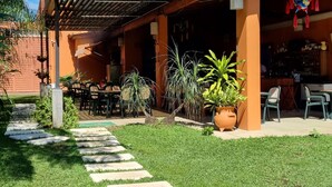 Uma área de pátio com mobiliário de exterior, uma pérgula e diversos vasos com plantas.
