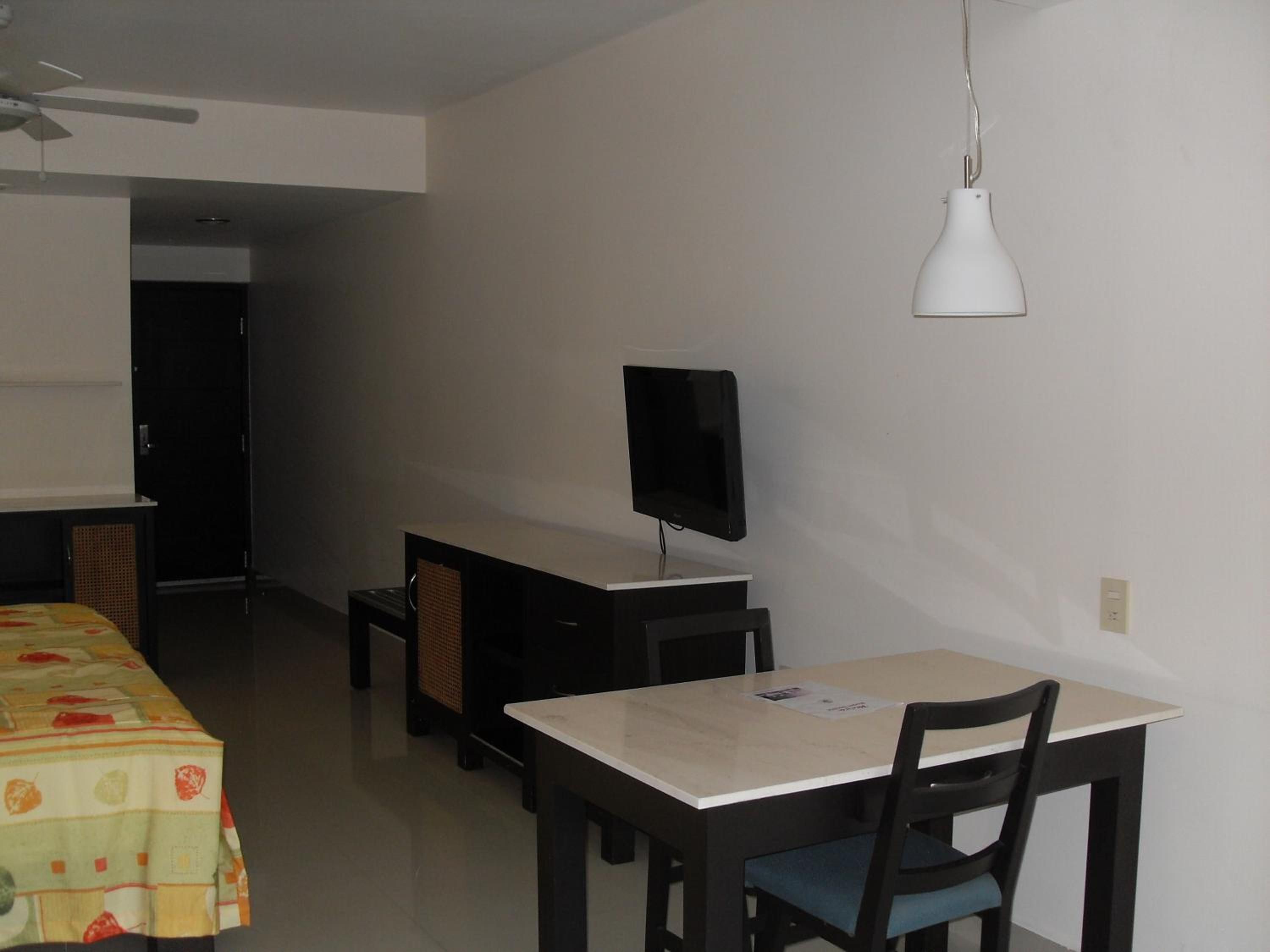 A room with a dining table, chairs, a television, and a ceiling fan.