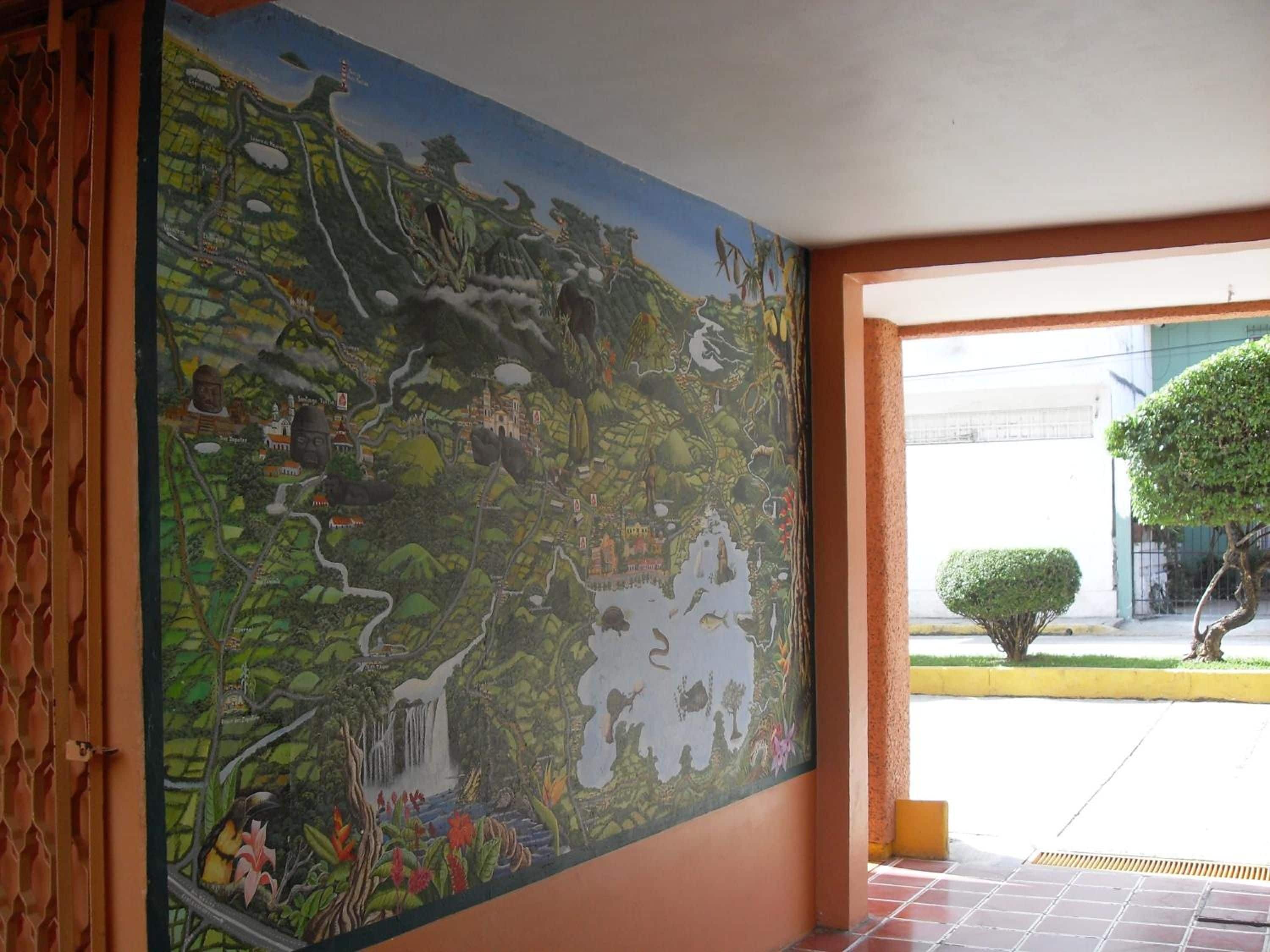 Un mural con un paisaje y edificios, una puerta con diseño decorativo y vista al exterior.