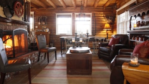 Acogedor interior de cabaña de troncos con chimenea, muebles de cuero y vigas de madera.