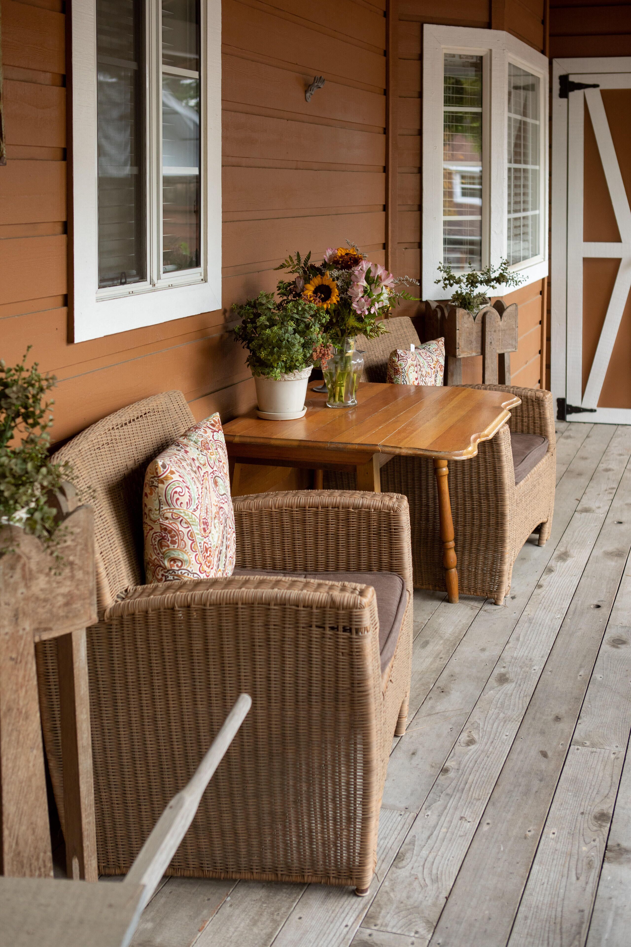 A wooden porch with wicker furniture, a table, and a potted plant.
