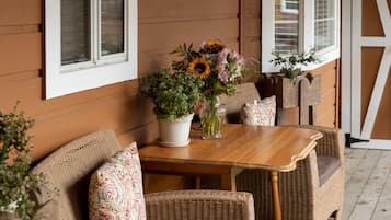 A wooden porch with wicker furniture, a table, and a potted plant.