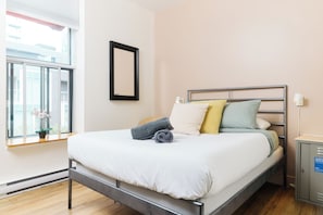 A modern bedroom with a metal bed frame, a large window with blinds, and a potted plant on the windowsill. - Auberge Saintlo Montréal  - Hostel (Montreal)