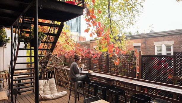 Una terraza en la azotea con cubierta de madera, una silla colgante y una mesa con una persona sentada.