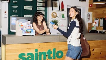 A reception desk with a sign reading 'saintlo' and a woman holding a postcard.