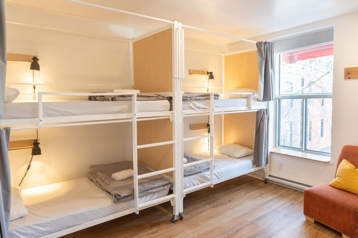 A dormitory room with bunk beds, a window with a view, and a small seating area.