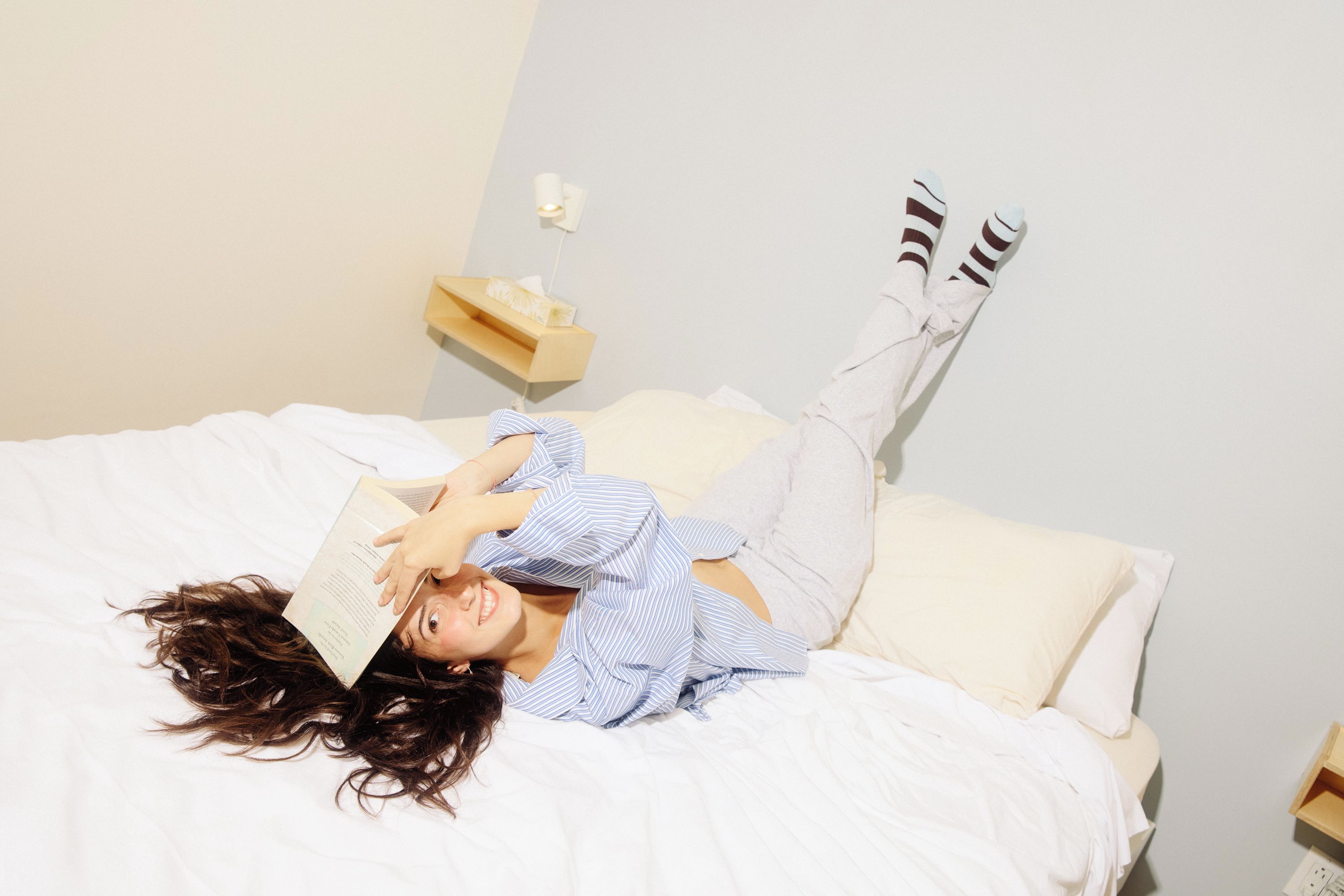 A person lying on a bed with a book, wearing striped shirt and striped socks.