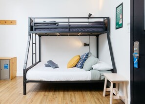 Una cama litera con escritorio y silla, un archivador pequeño y una lámpara de pared.