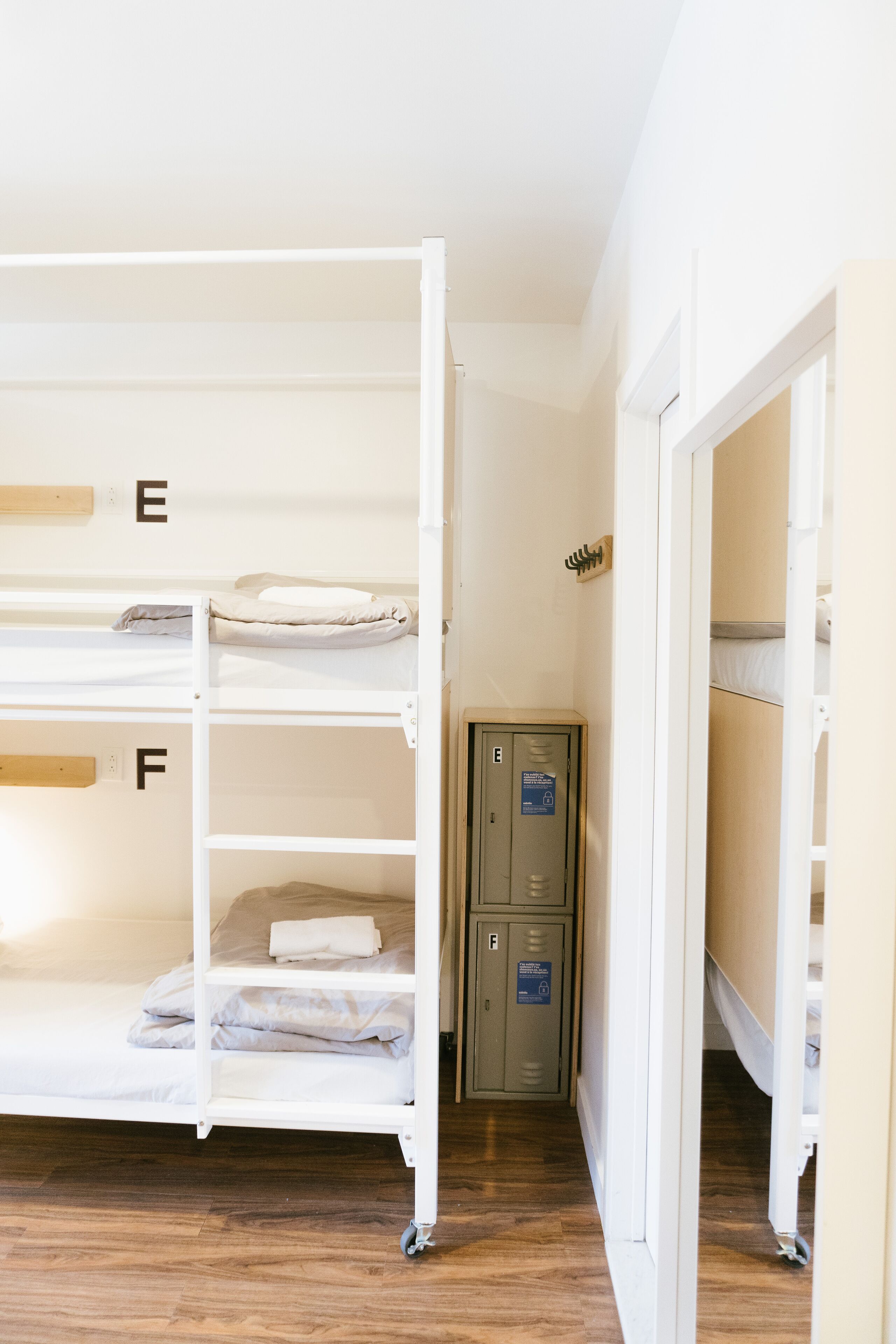Une chambre avec des lits superposés, les lits étant identifiés par les lettres E et F, ainsi qu’un meuble de rangement et un plancher en bois.