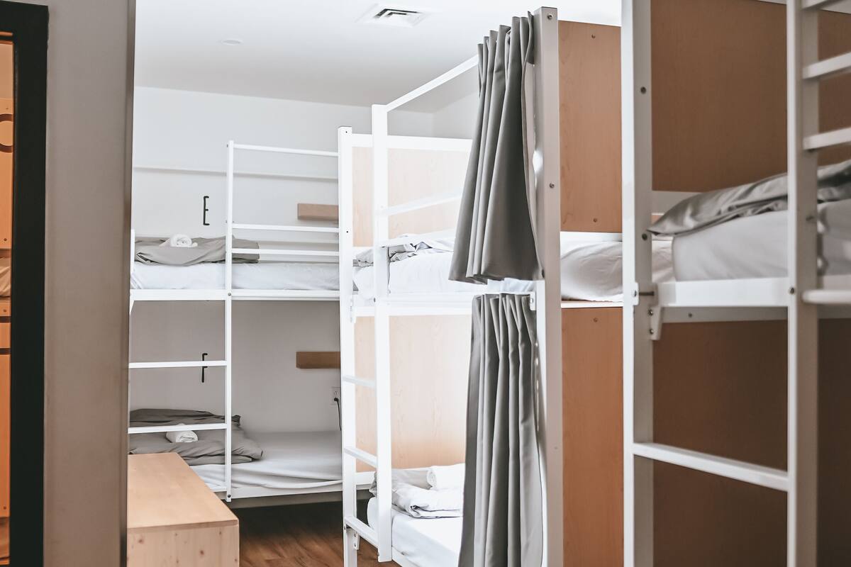 A dormitory room with bunk beds, wooden flooring, and a small desk.