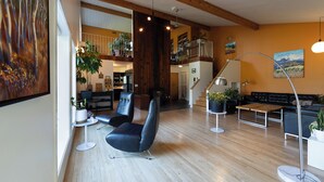 A spacious living area with a wooden floor, black leather chairs, a wooden coffee table, and a modern floor lamp. There is a staircase leading to an upper level with a balcony. - Boréale Ranch (Whitehorse)