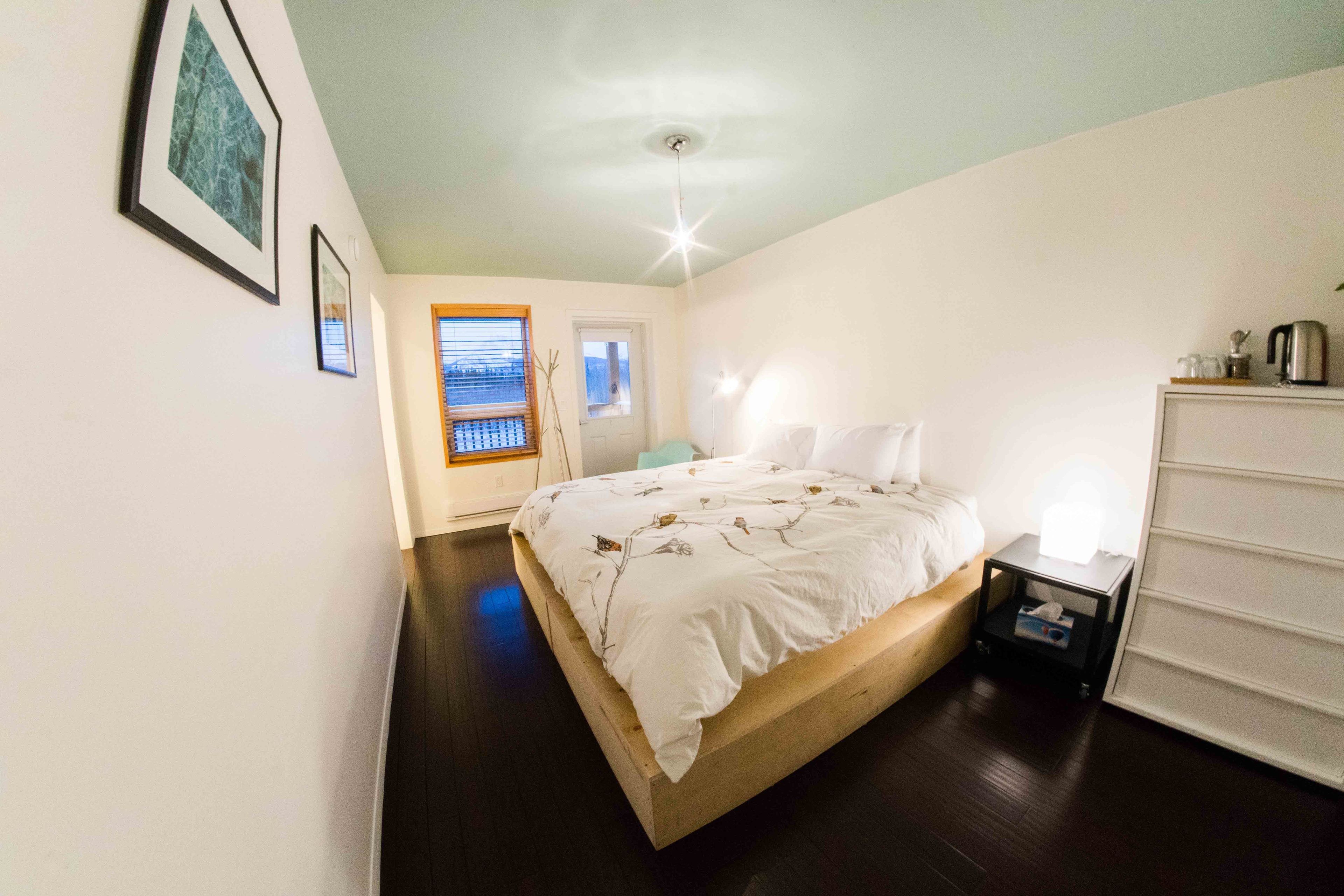 Un dormitorio con cama de madera, paredes blancas y una lámpara en el techo.