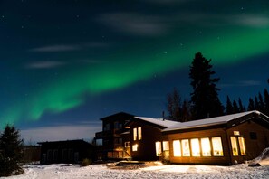 Una cabaña con el suelo cubierto de nieve, fachada de madera y un interior iluminado.