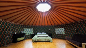 A spacious room with a high ceiling and a central skylight, a bed, a sofa, and a small table with a lamp. - Boréale Ranch (Whitehorse)