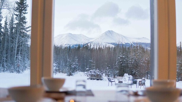 A dining area with a view of snow-covered mountains and trees. - Boréale Ranch (Whitehorse)