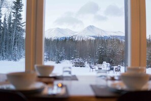 A dining area with a view of snow-covered mountains and trees. - Boréale Ranch (Whitehorse)