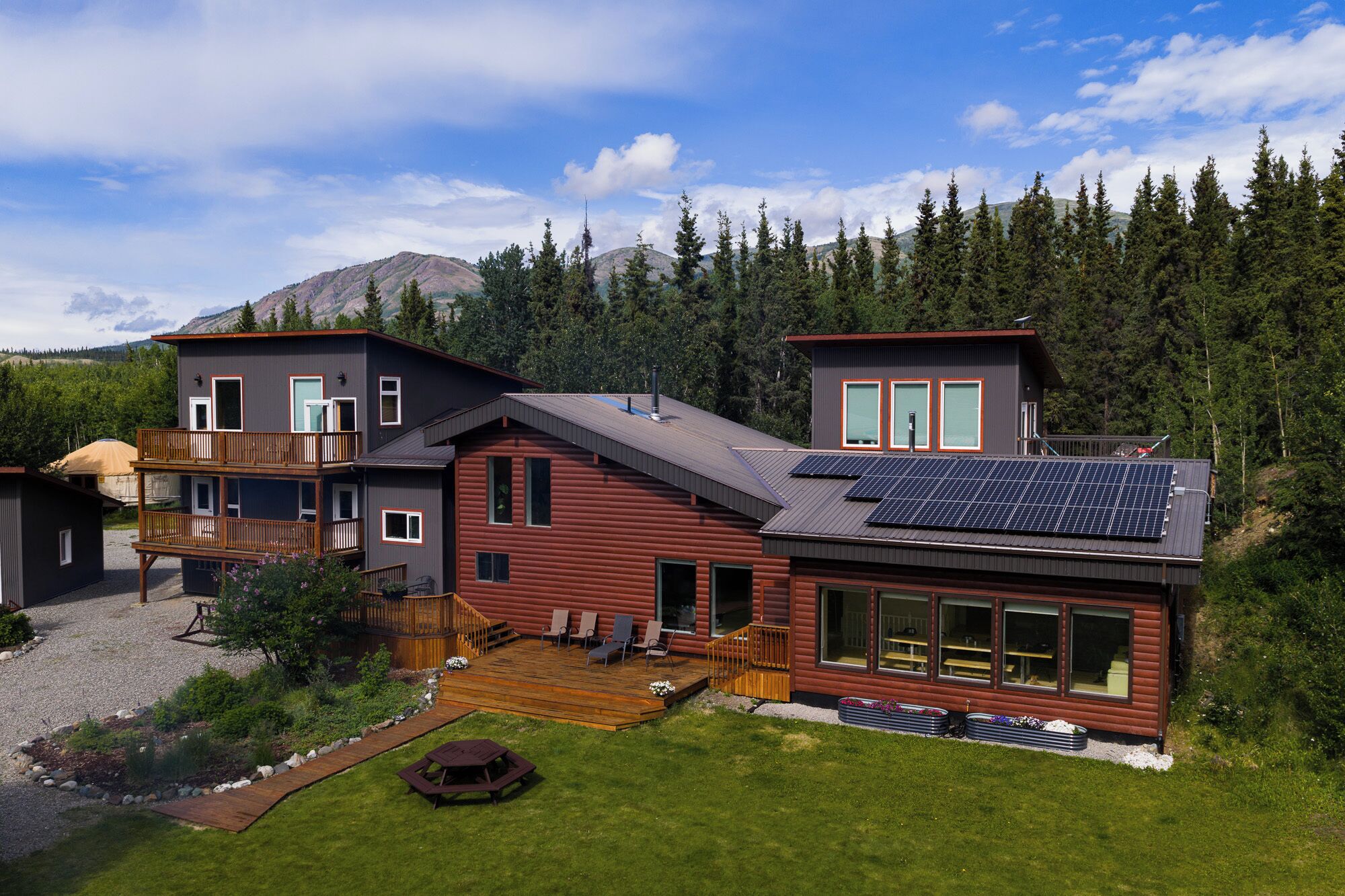 A modern log cabin with a deck, large windows, and solar panels.